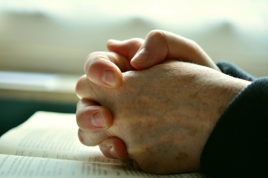 A imagem representa as mãos  entrelaçadas de uma pessoa que está rezando.